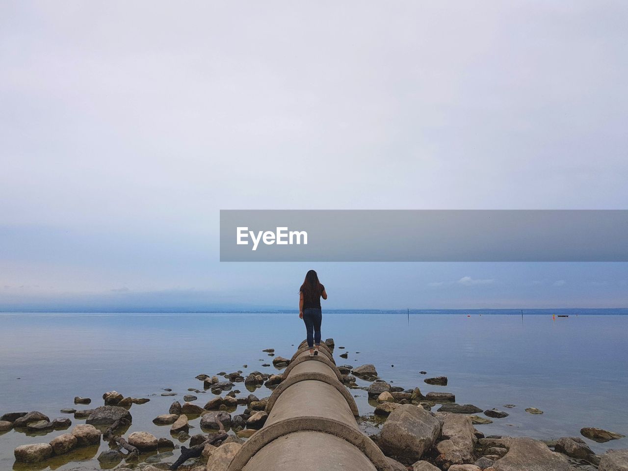 Woman walking on pipe at beach against sky