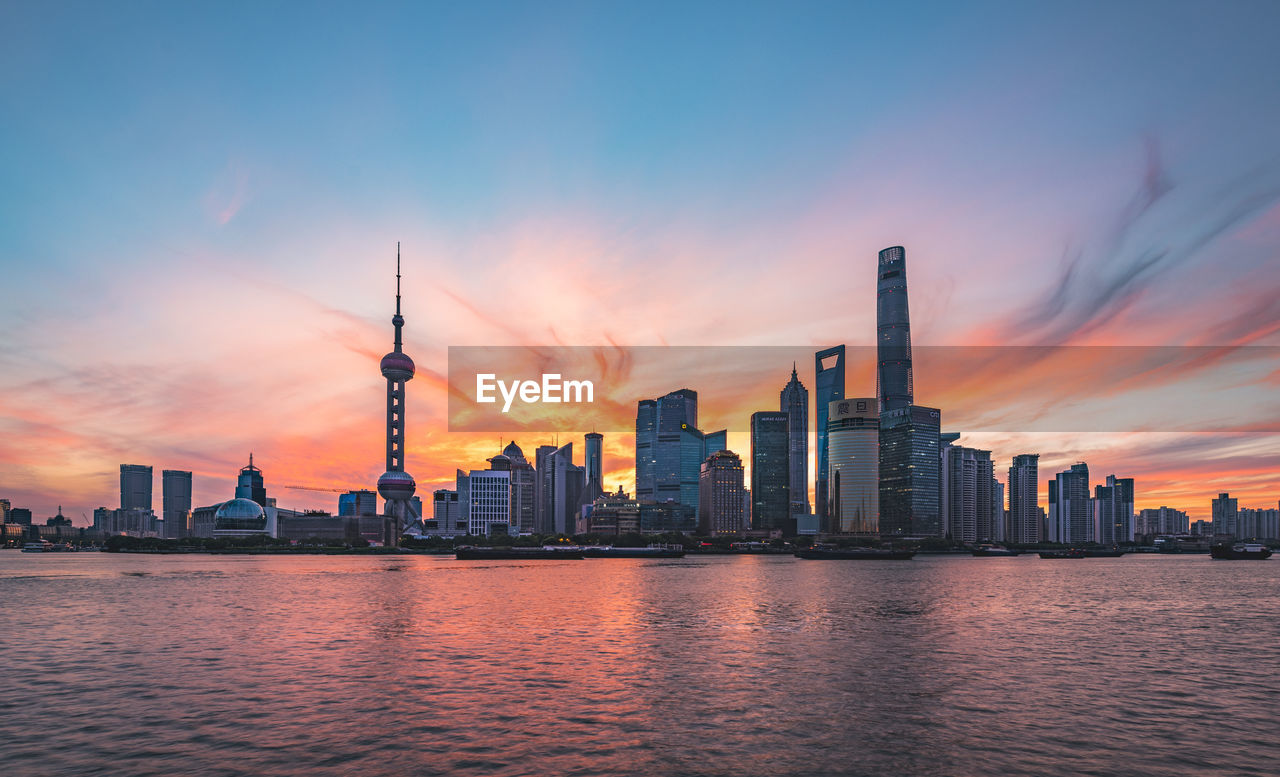 Modern buildings and river against sky during sunset