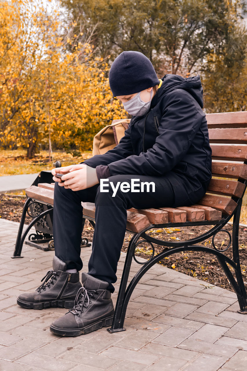 Schoolboy in a protective mask sits on a bench and holds a smartphone. new normal.