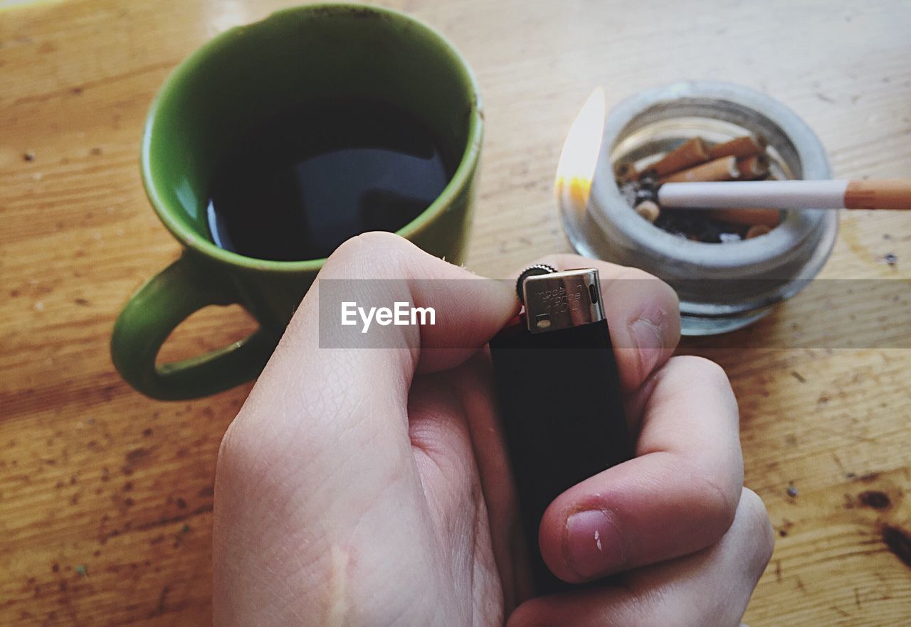 Cropped hand holding lit cigarette lighter on wooden table
