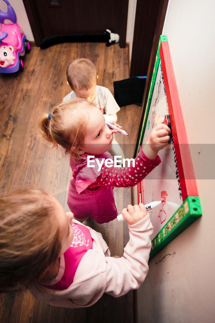 High angle view of siblings writing on whiteboard at home