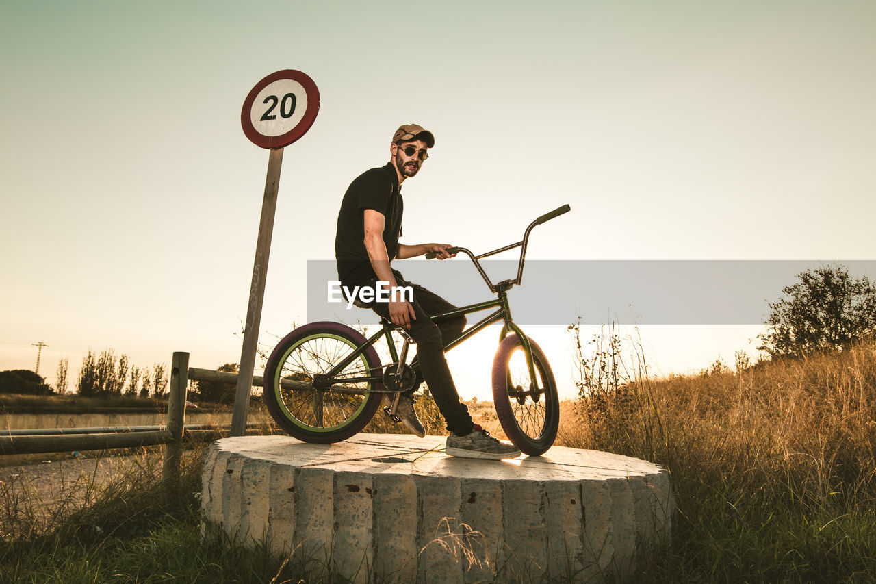 Side view of young man with bicycle against clear sky during sunset