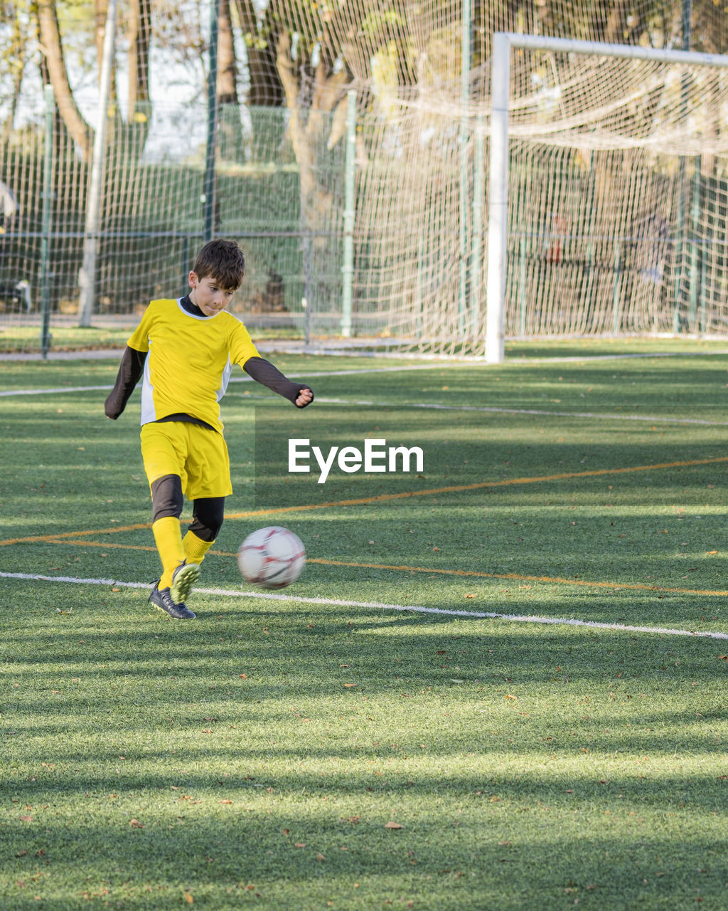 Football player in yellow uniform shooting the ball during a match.