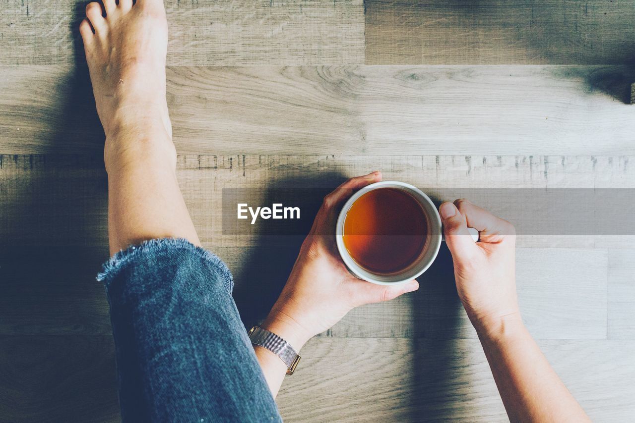 Low section of woman holding coffee cup on floor