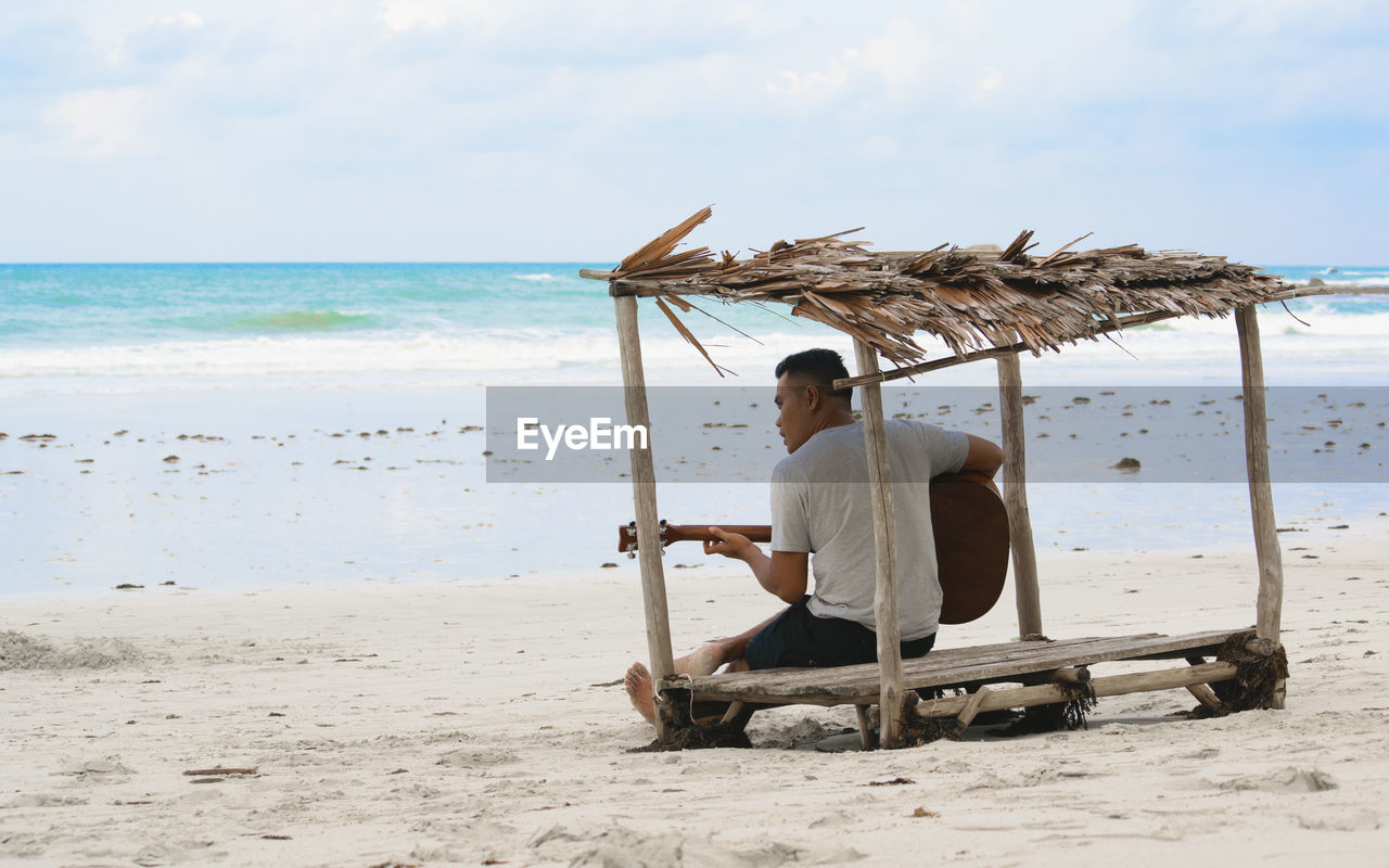 Rear view of man playing guitar on beach against sky