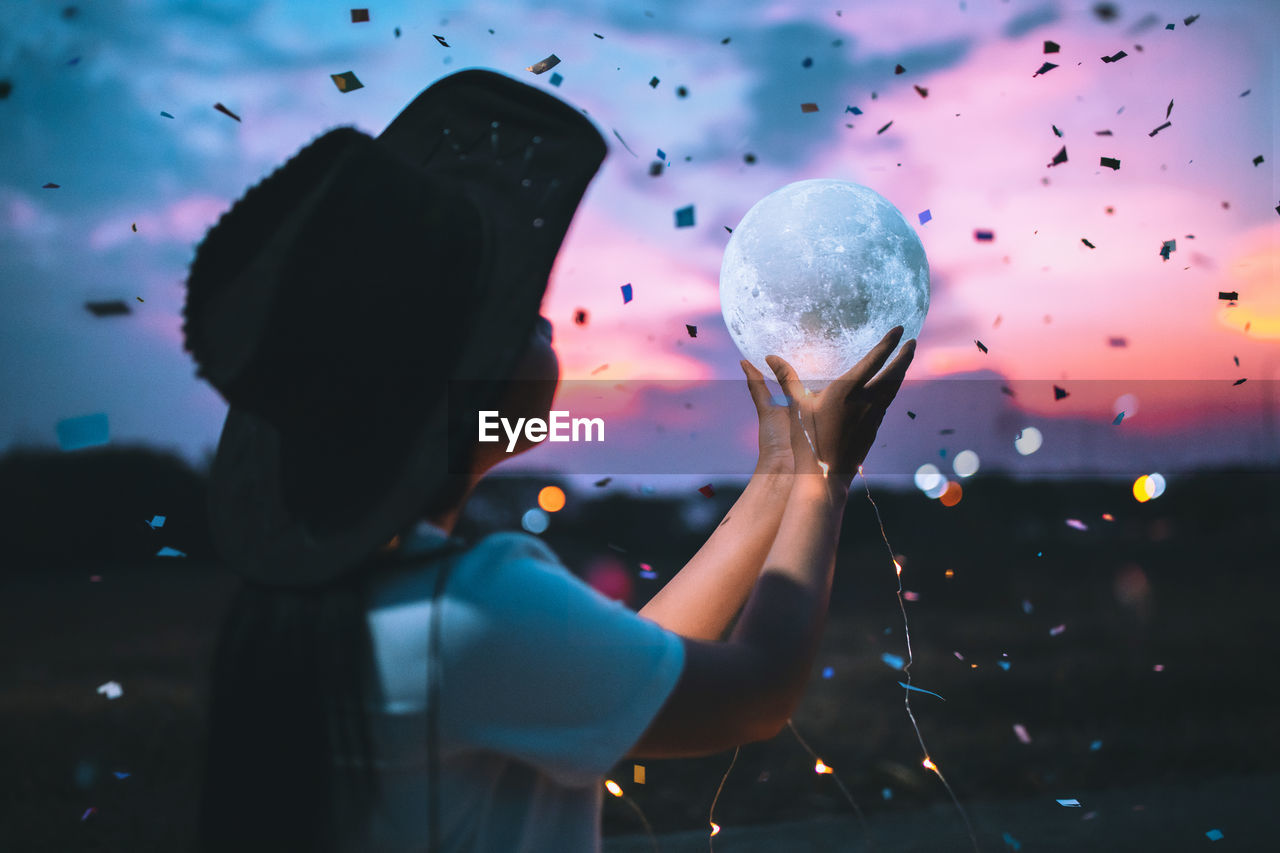 Girl holding crystal ball against sky during sunset