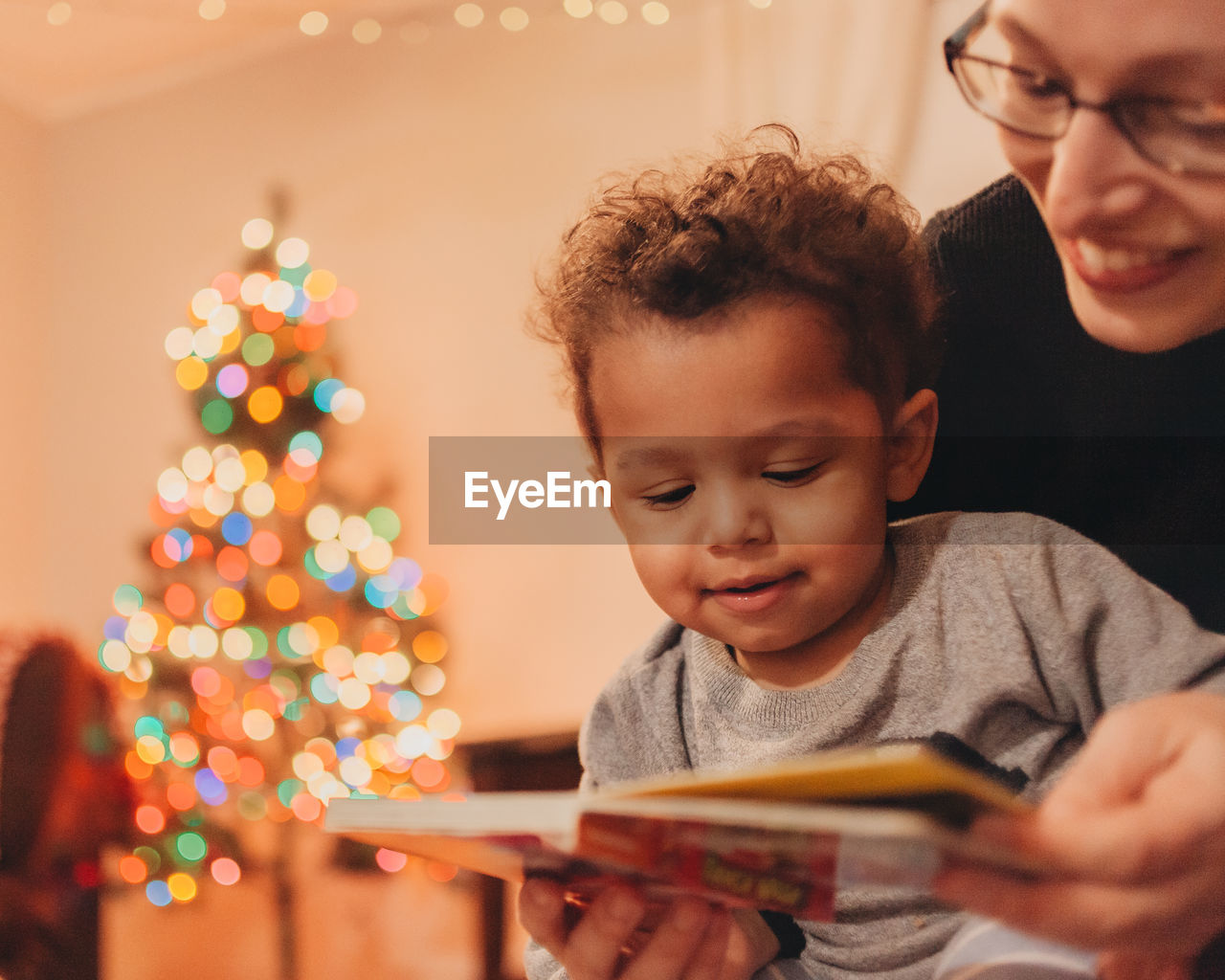 Close-up of mother with baby son reading book at home during christmas