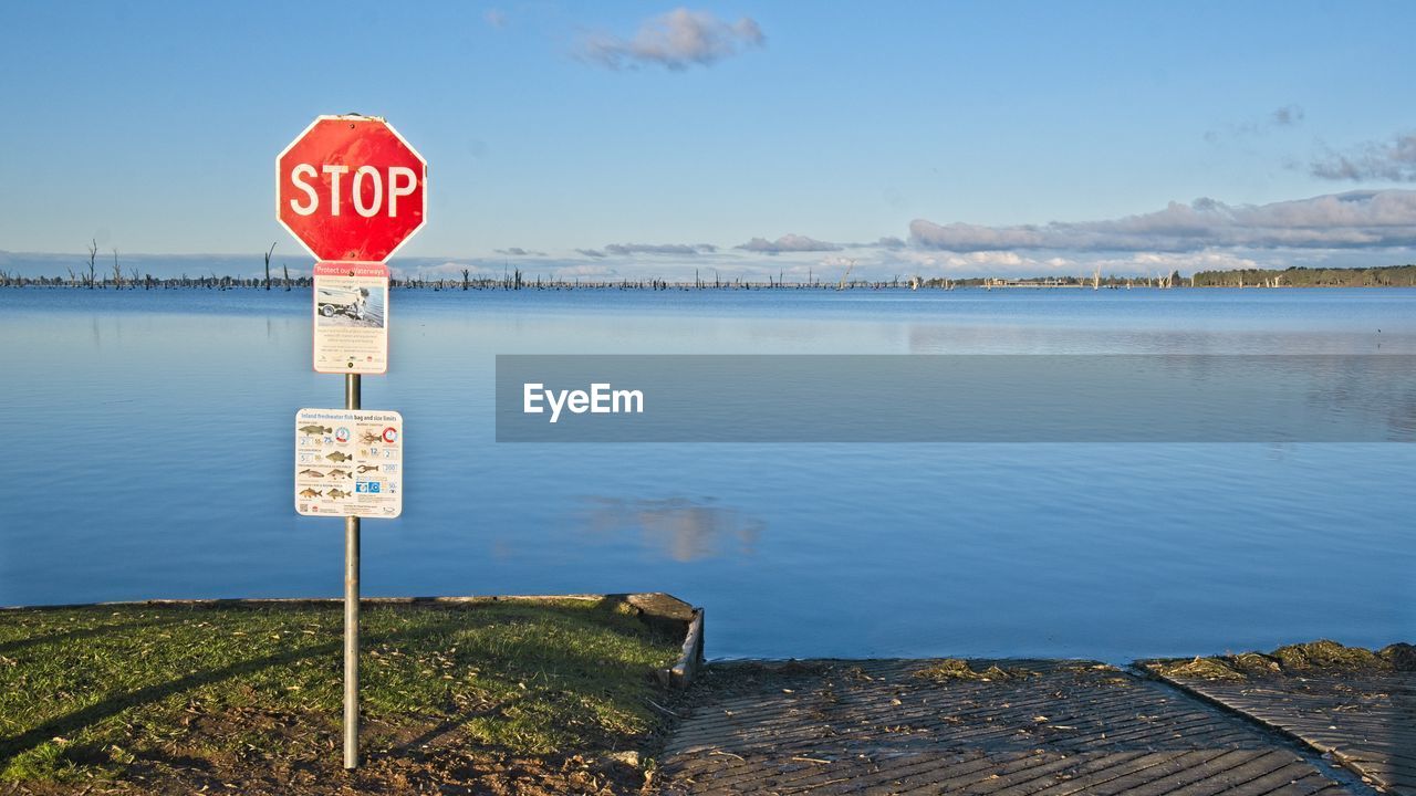 ROAD SIGN BY LAKE AGAINST BLUE SKY