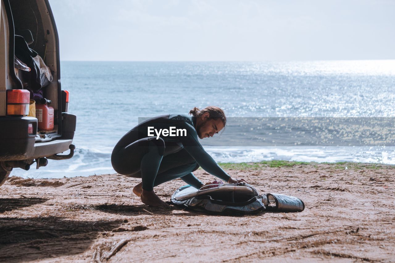 SIDE VIEW OF YOUNG MAN SITTING AT BEACH