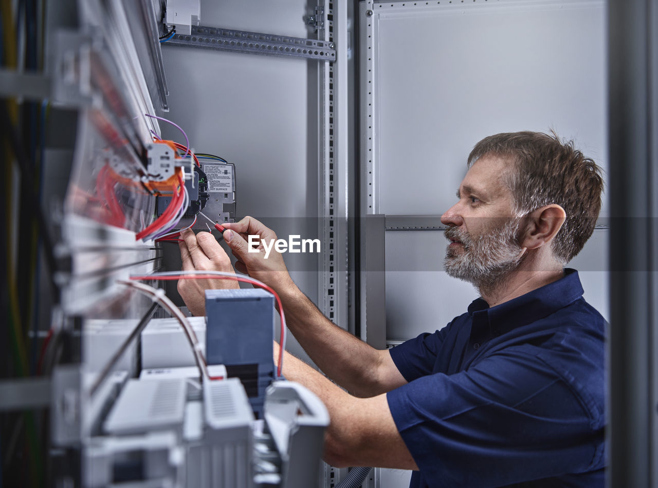 Male electrician examining power supply in electrical workshop