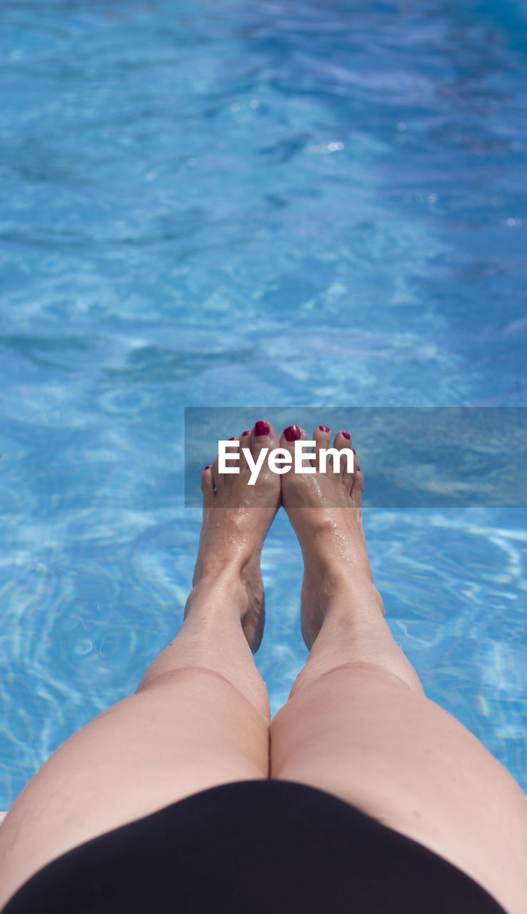 LOW SECTION OF WOMAN LEGS SWIMMING IN POOL