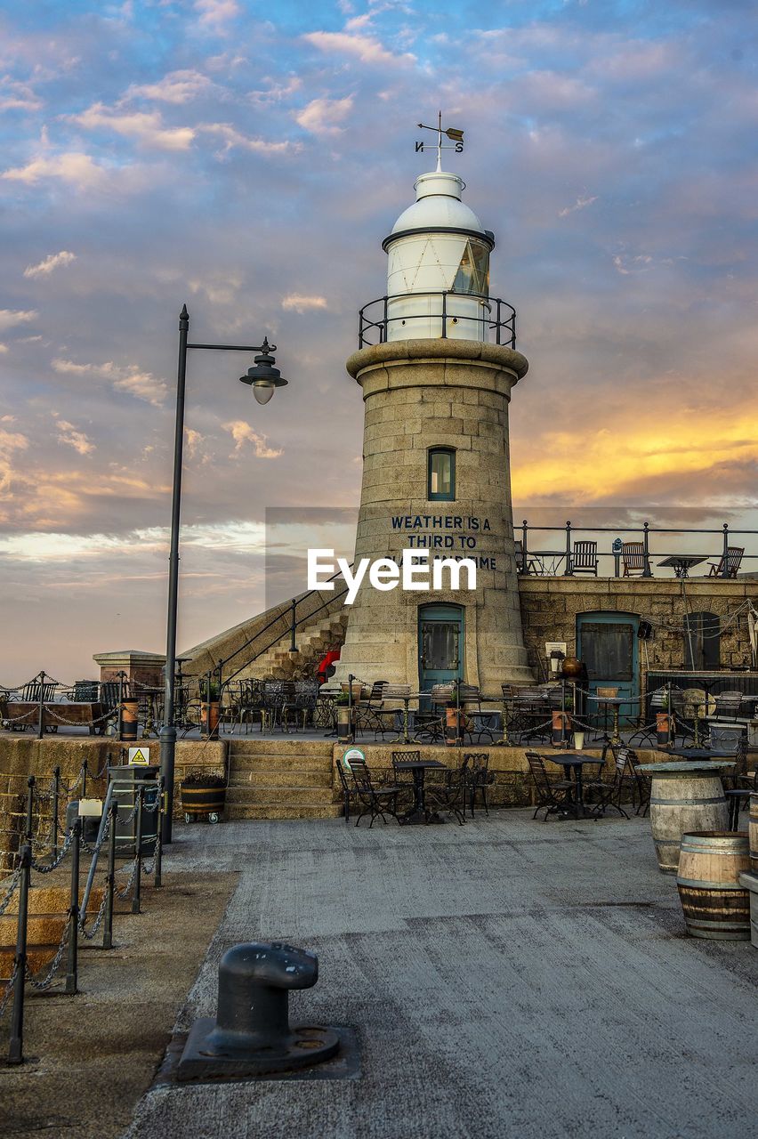 Lighthouse by buildings against sky at sunset