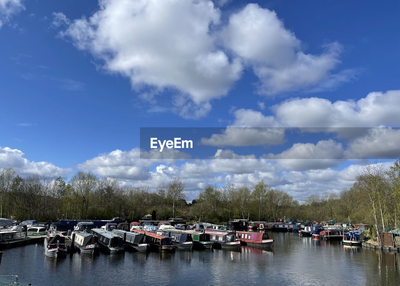 BOATS MOORED IN RIVER BY TREES AGAINST SKY