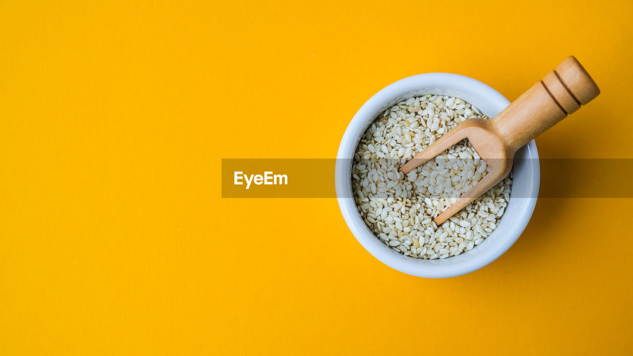 Wooden spoon with sesame seeds lies in a white mortar on a yellow background. healthy eating. keto 