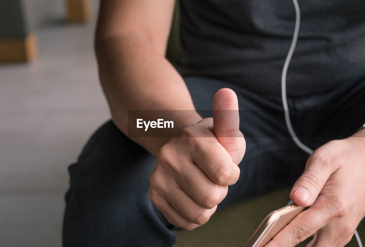 Midsection of man with phone showing thumbs up