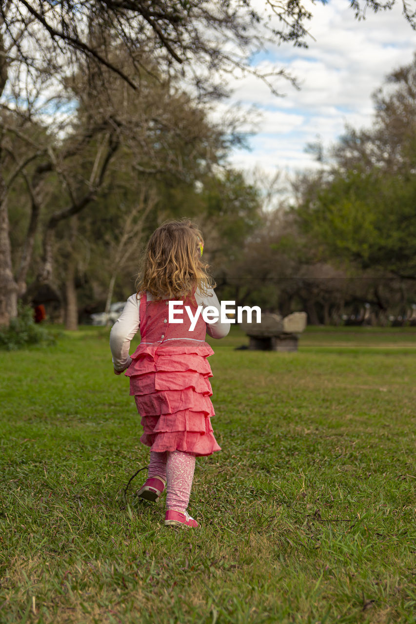 Rear view of girl running on grass against trees