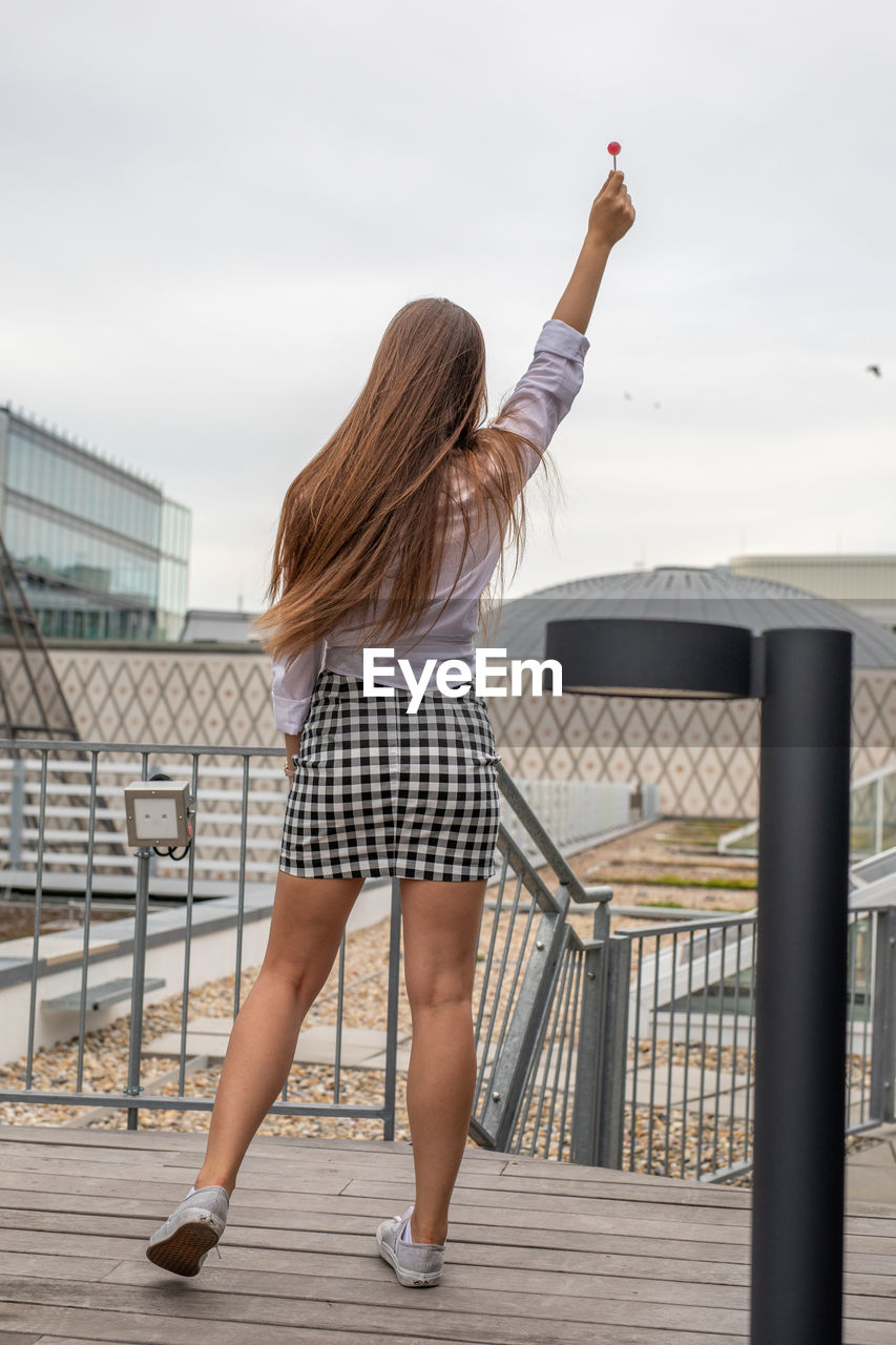 Rear view of woman with lollipop standing on boardwalk against sky