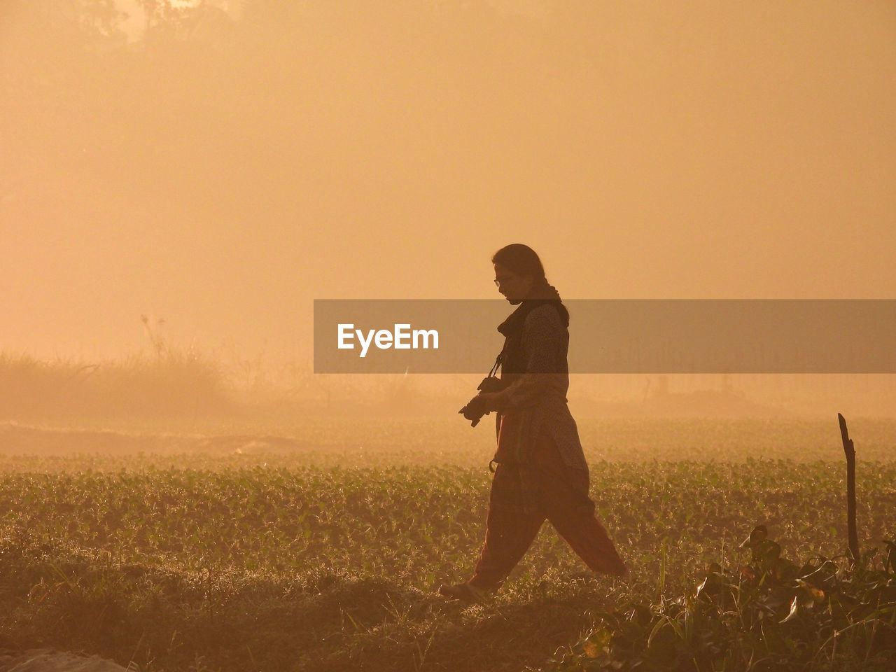 Side view of silhouette woman standing on field against sky during sunrise 