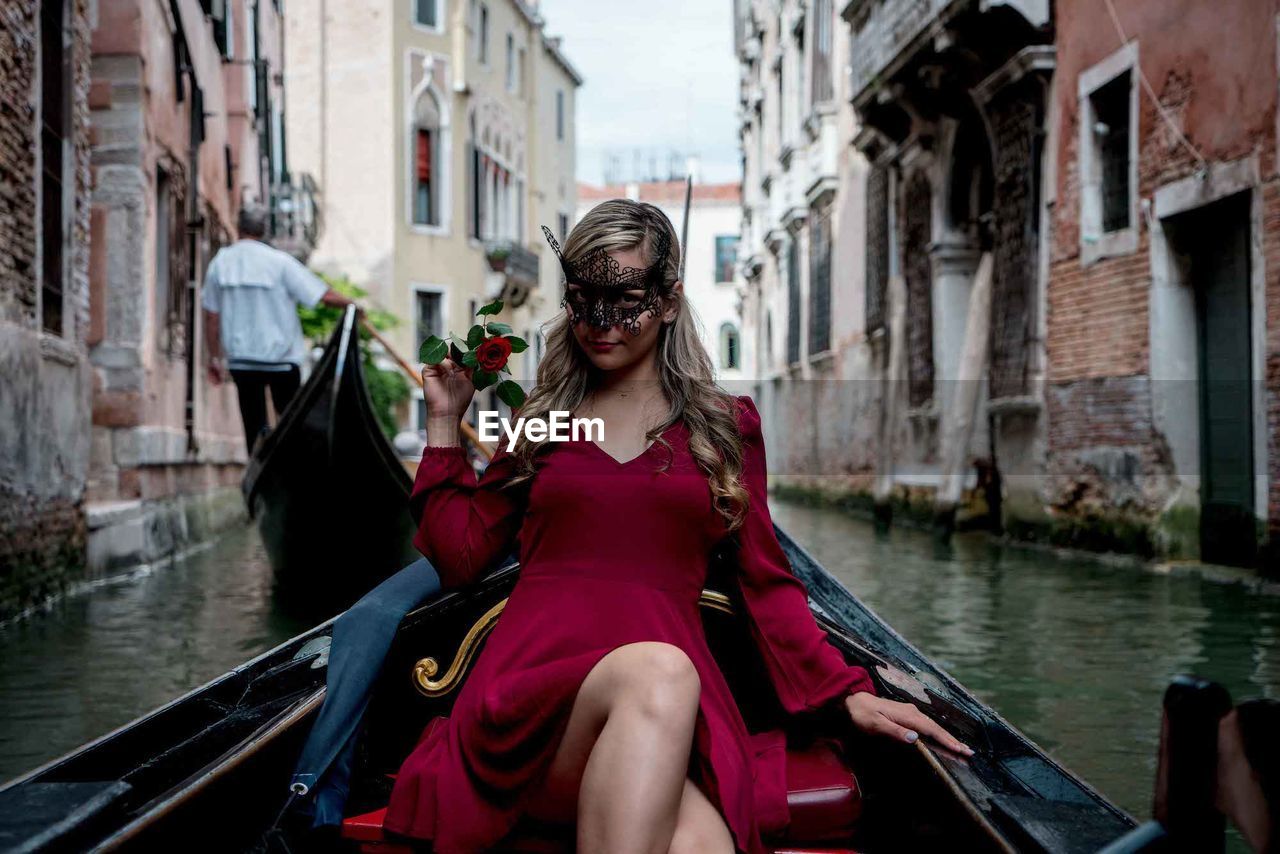 Portrait of smiling woman wearing mask while sitting on gondola in canal