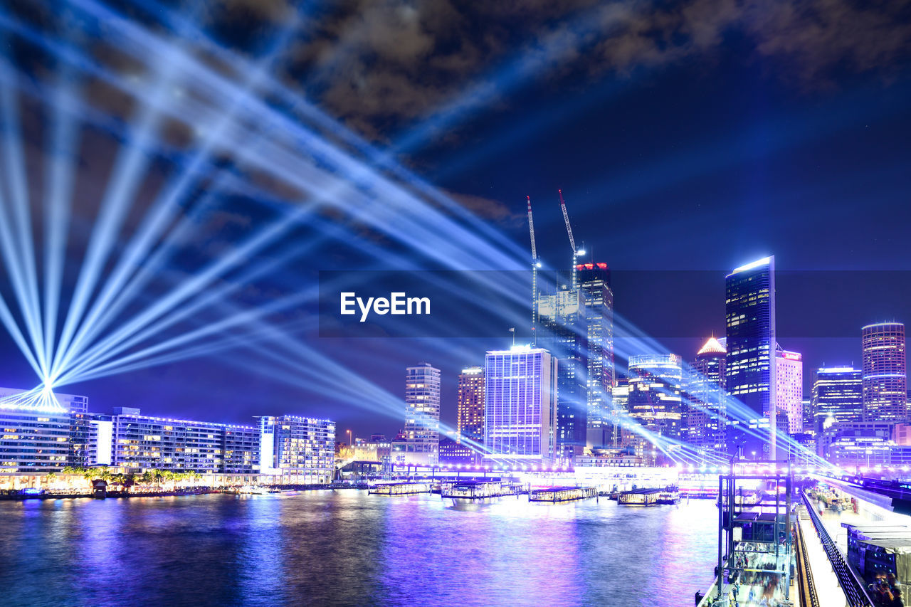 ILLUMINATED BRIDGE OVER RIVER AND BUILDINGS AGAINST SKY