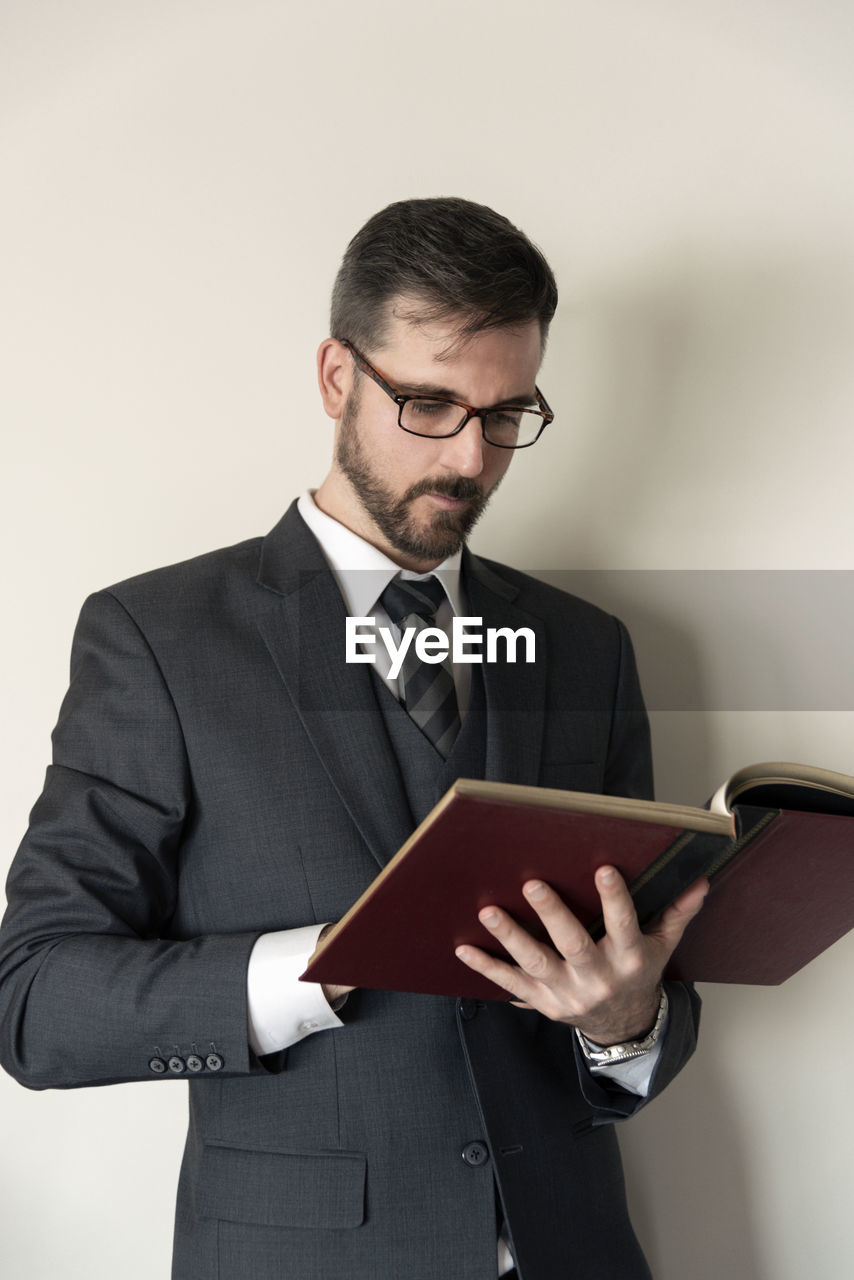 Businessman reading book while standing against wall