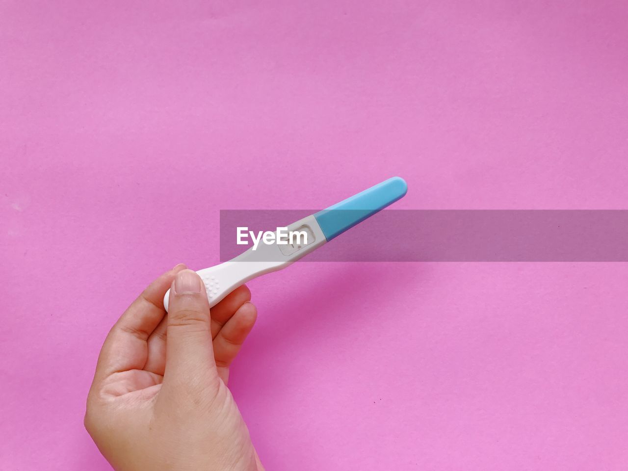 Close-up of hand holding pregnancy test over pink background