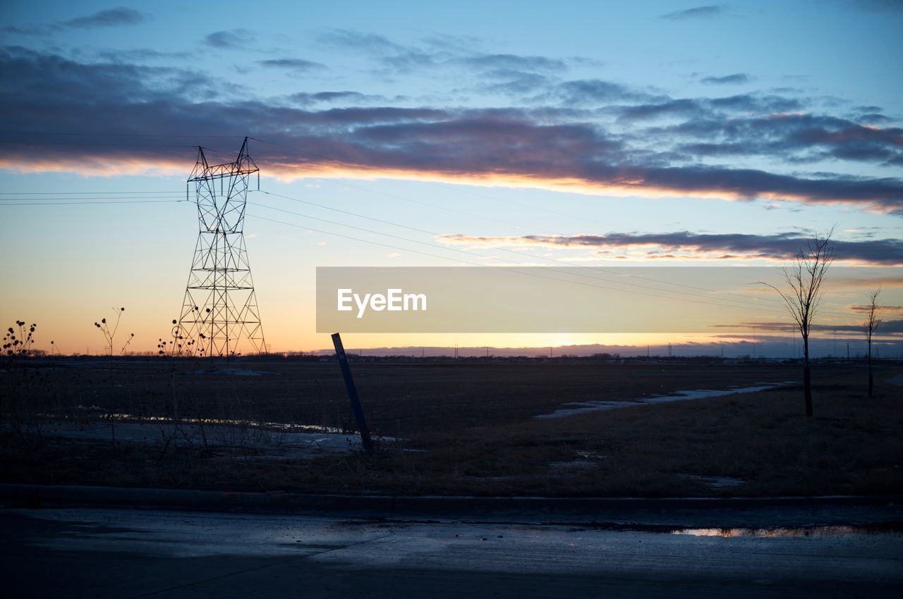 ELECTRICITY PYLONS ON LANDSCAPE AT SUNSET