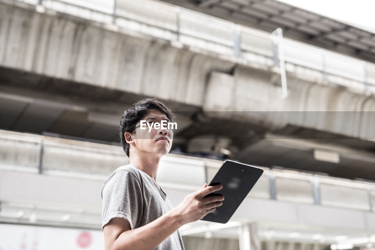 Low angle view of man holding digital tablet while standing in city