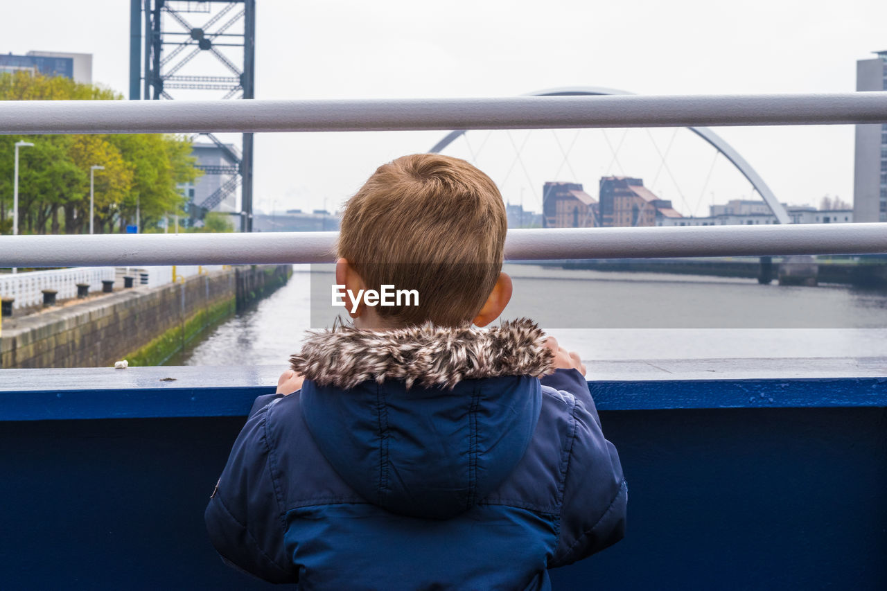 Rear view of boy standing on bridge over river