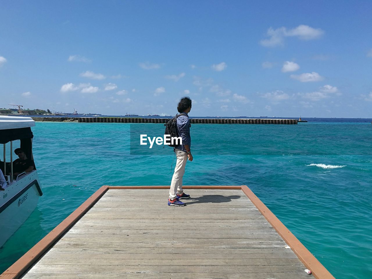Full length side view of man standing on pier over sea against sky during sunny day