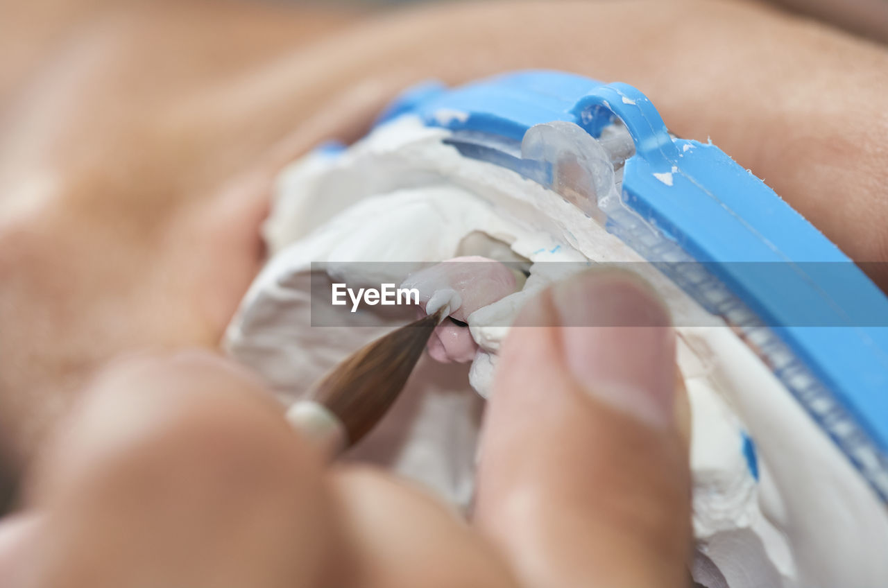 Close-up of person using paintbrush while molding dentures