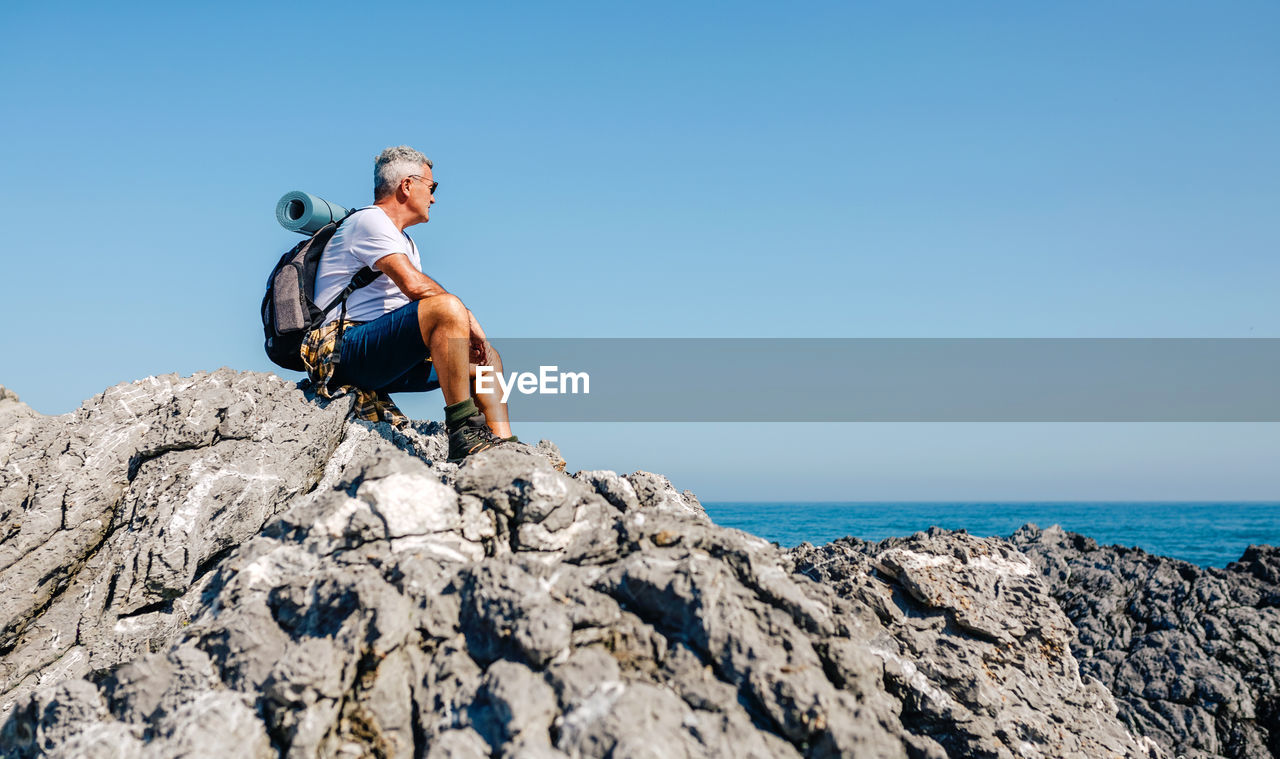 Senior man hiking looking at sea landscape sitting on rocks
