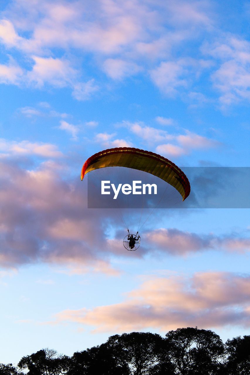 Low angle view of man powered paragliding against sky