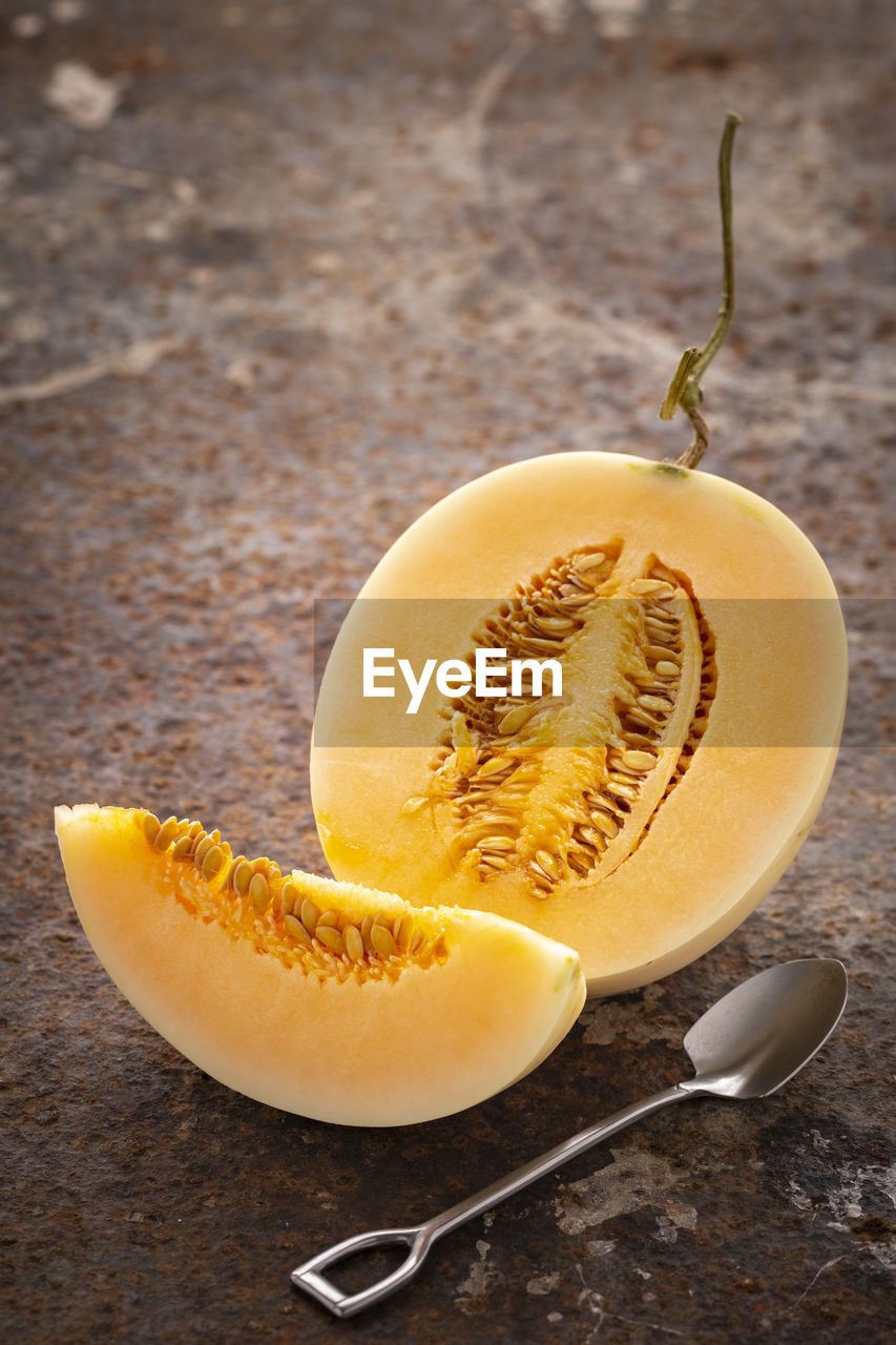 Sliced yellow cantaloupe melon with dessert spoon on rusty texture background