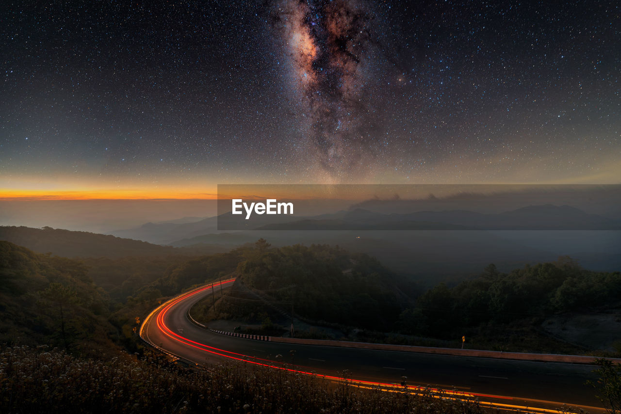 Light trails on road against starry sky at night