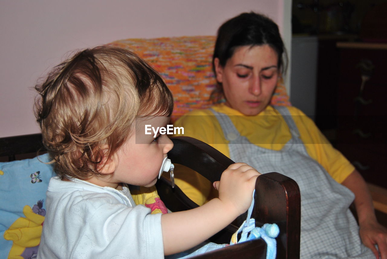 Cute baby boy sucking pacifier with mother at home