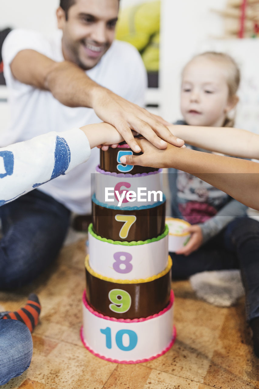 Cropped image of teacher and students piling up hands on number blocks