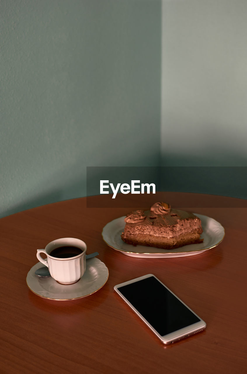 Coffee cup, a cupcake and phone on a corner table. conceptual image