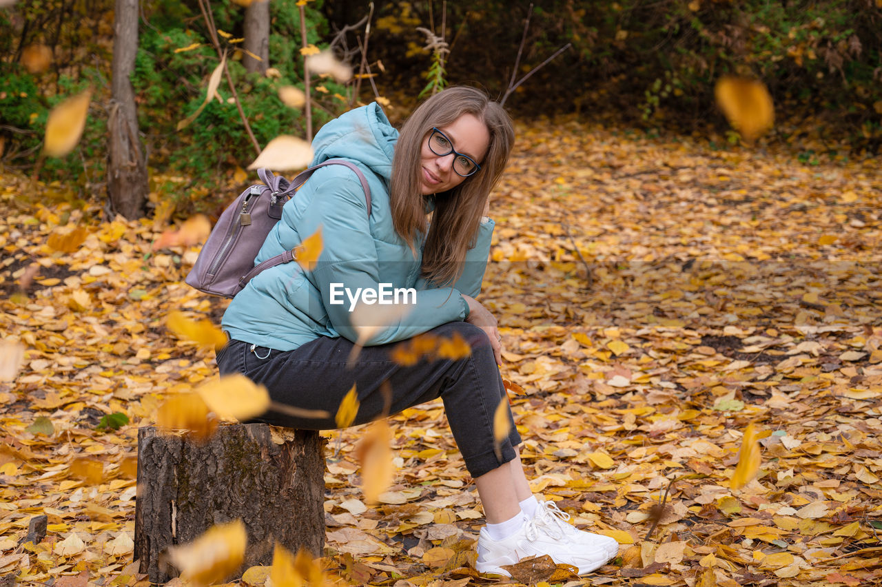 PORTRAIT OF YOUNG WOMAN WITH AUTUMN LEAVES ON ROAD