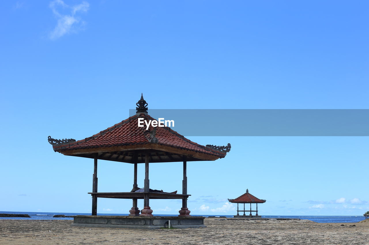 Gazeboes at beach against blue sky