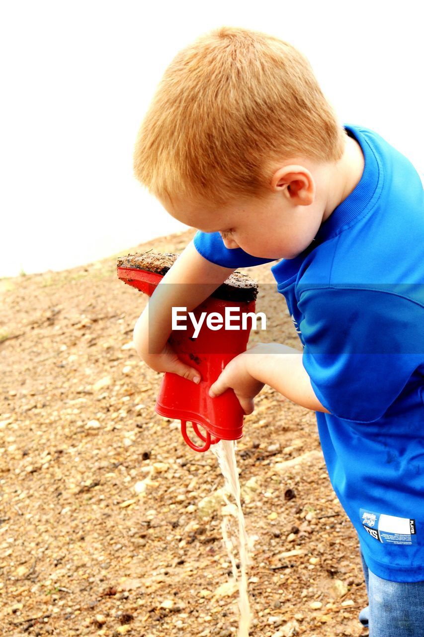 Boy pouring water from boot to sand