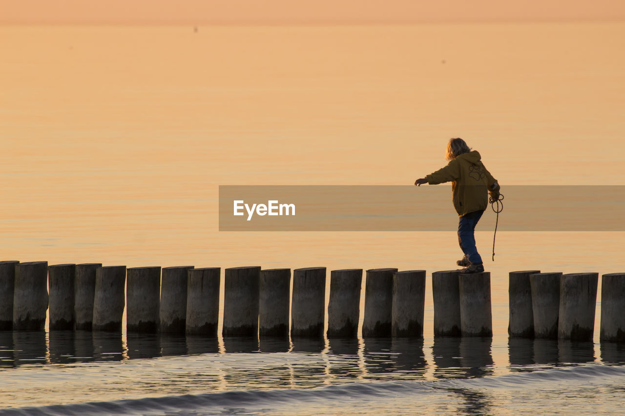 REAR VIEW OF MAN STANDING ON PIER OVER SEA