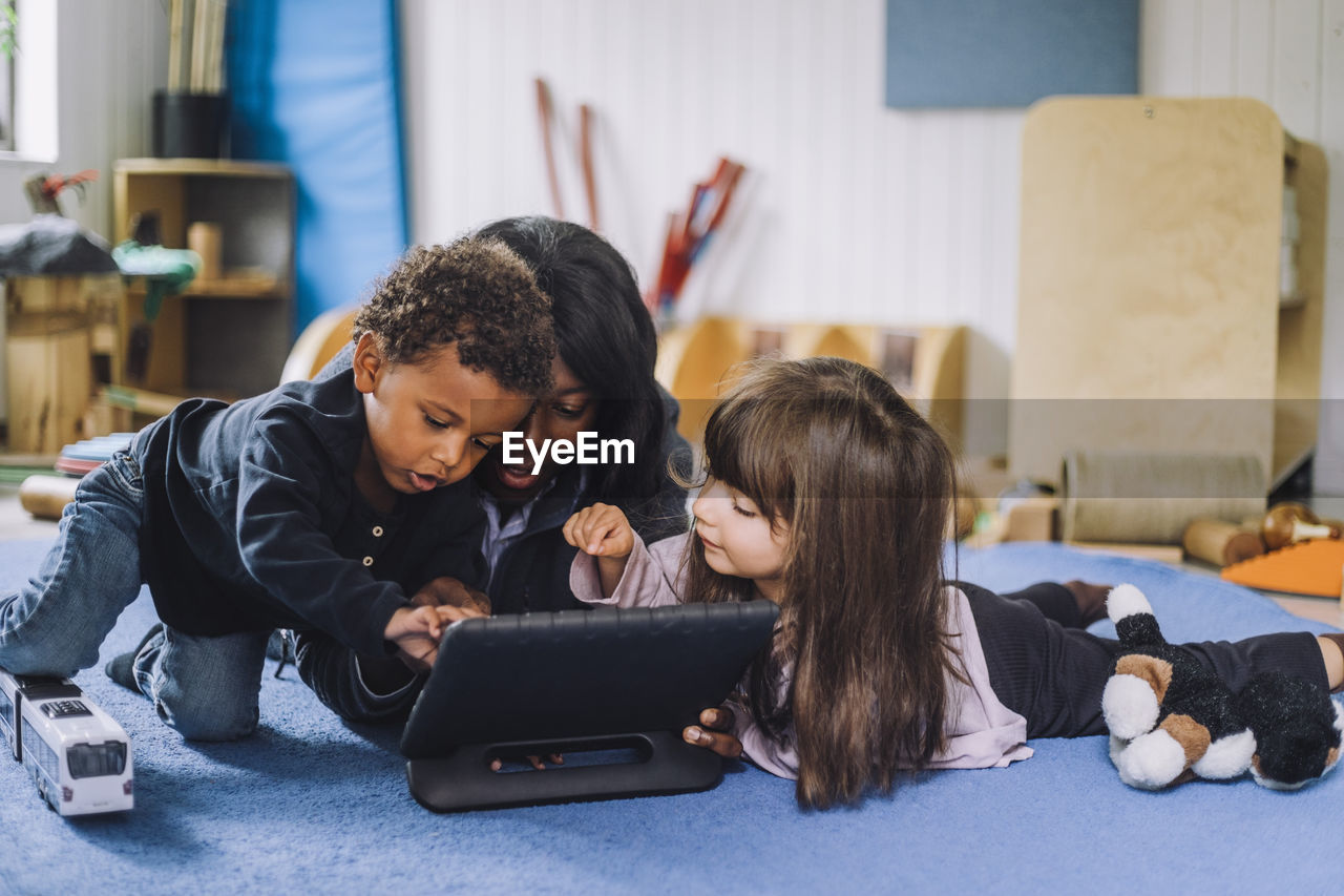 Female teacher sharing digital tablet with children in child care center