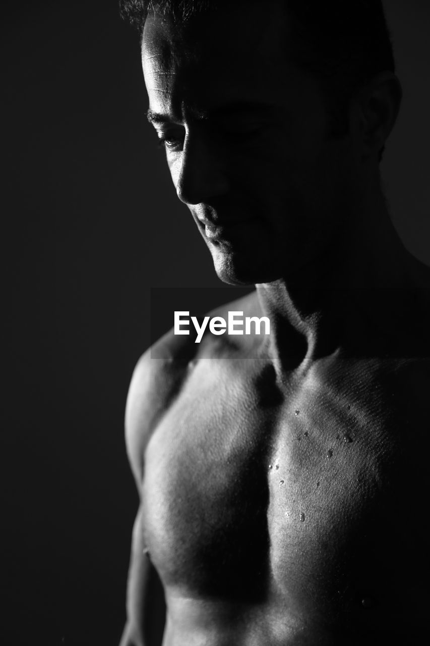 Close-up of shirtless man against black background