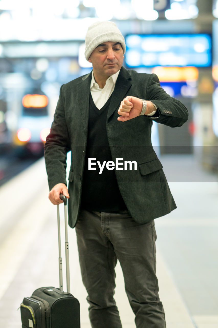 Man checking time while standing with luggage on railroad station platform