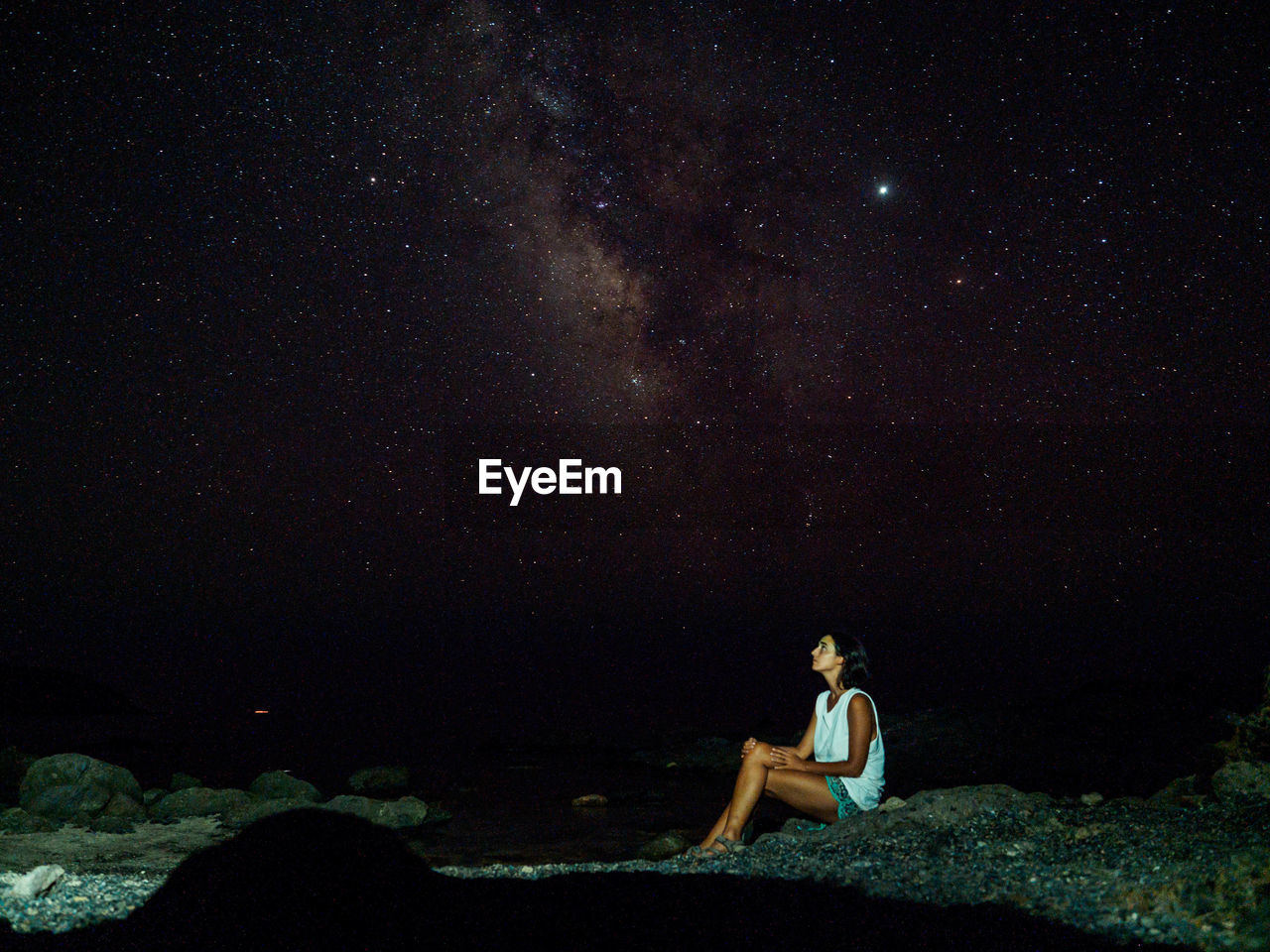 Young woman sitting on rock against star field at night