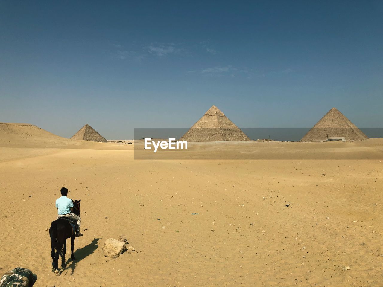 REAR VIEW OF MAN RIDING IN DESERT AGAINST SKY