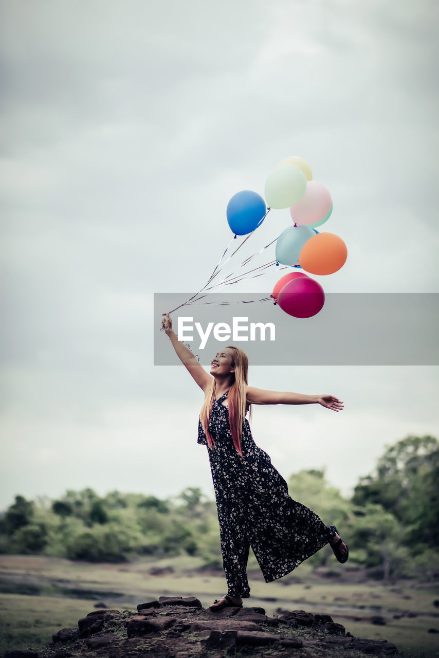 REAR VIEW OF WOMAN WITH BALLOONS AGAINST SKY