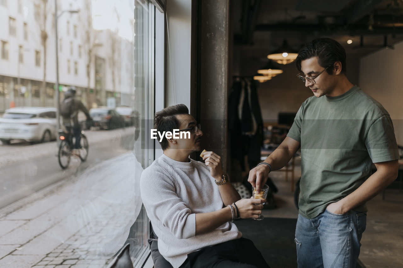 Businessman talking with male colleague while having cookie in break at startup company