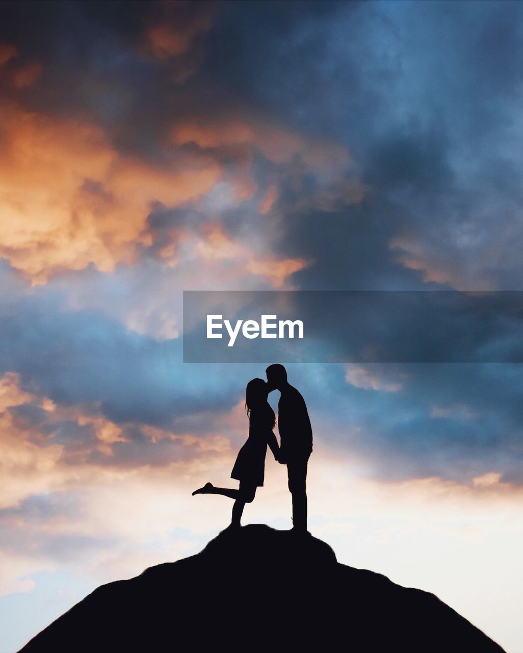 Low angle view of silhouette man kissing woman while standing against sky during sunset